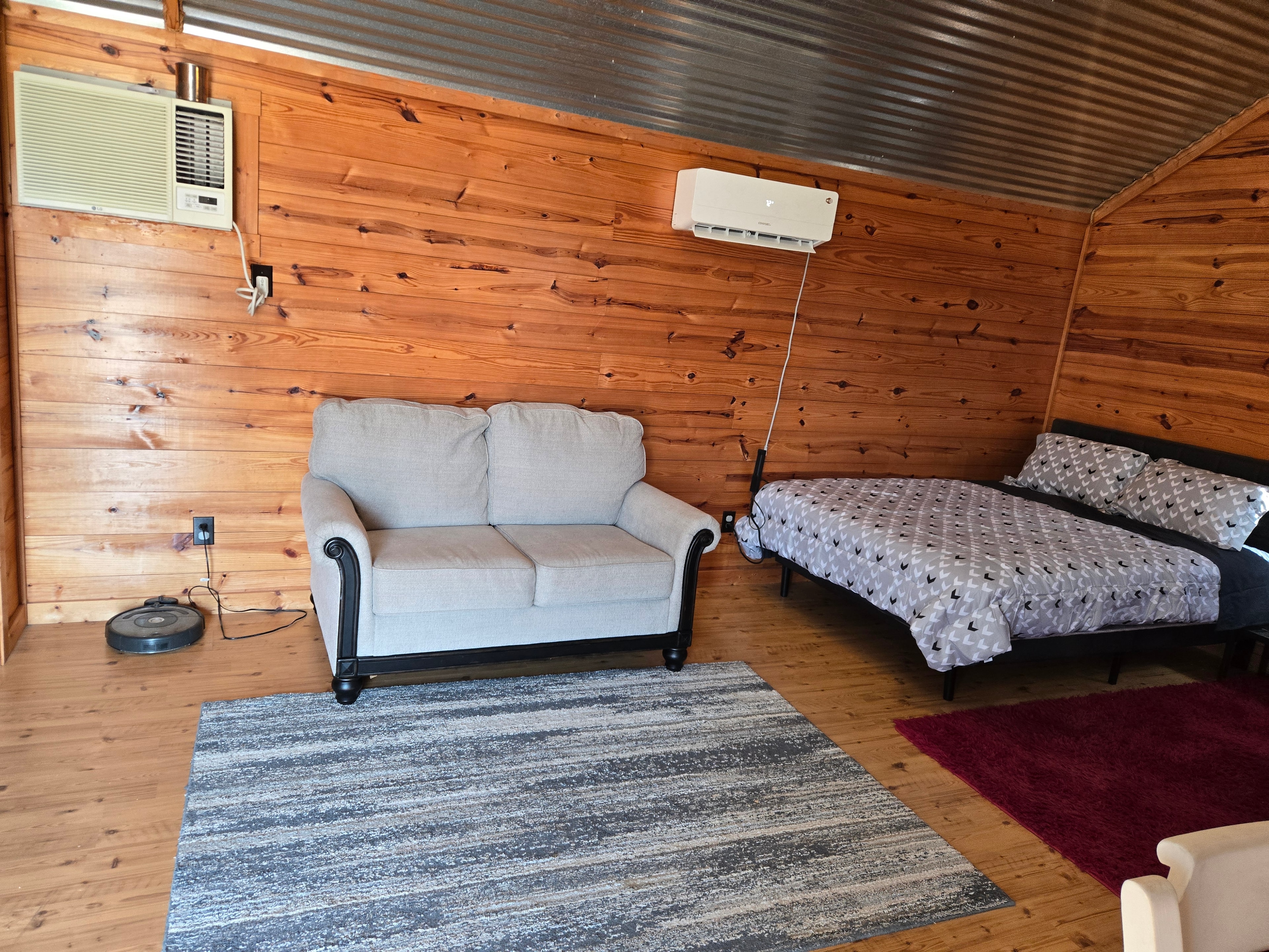 Cabin living area with loveseat, queen bed, and A/C unit